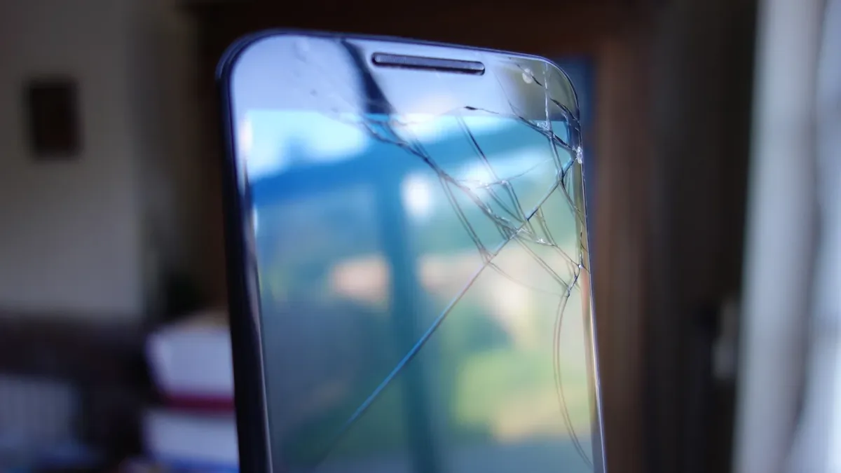 Nahaufnahme eines Smartphones mit gesprungenem Display, das Glas von der oberen Ecke quer über den Bildschirm zersplittert.